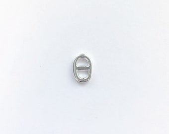 Pode incluir: Fecho de correr de metal prateado, uma pequena peça de joalheria de forma oval com um laço de cada lado.
