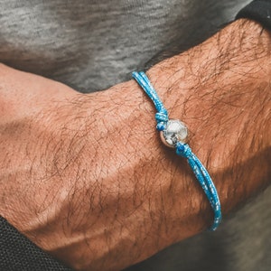 Peut inclure: Un bracelet en corde bleu et blanc avec un charme de ballon de football argenté.
