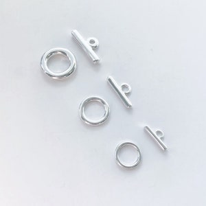 Può includere: Tre set di chiusure a scatto argentate con anelli. Ogni set include una barra con un anello e un anello.