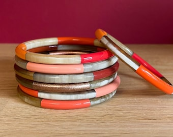 Pode incluir: Uma pilha de pulseiras coloridas com uma mistura de detalhes laranja, vermelho, rosa e dourado. As pulseiras são feitas de um material natural com um acabamento liso e polido.