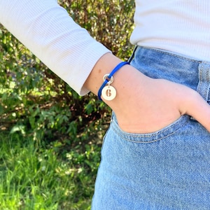 Pode incluir: Um bracelete de cordão azul com um berloque de prata com o número "6" recortado.