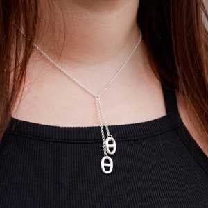 May include: A silver chain necklace with two dangling oval charms. The charms are in the shape of the letter "O" with a smaller circle inside.