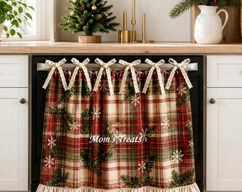 May include: A kitchen appliance cover featuring a red, green, and cream plaid pattern with printed pine branch and snowflake motifs. The fabric has a ruffled bottom edge and is attached with six cream-colored ribbon bows. The text Mom's Treats is visible.