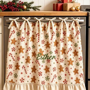 May include: A cream-coloured dishwasher cover featuring a repeating pattern of brown gingerbread men, red and white candy canes, and green stars. The fabric is secured with six tied bows at the top and has a ruffled bottom edge with the name Esther.