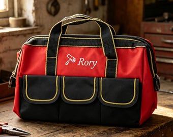 May include: A red and black tool bag with two black handles, featuring three front pockets with yellow trim and the white embroidered text "Rory" accompanied by a paint roller icon on the front panel of the durable fabric construction.