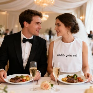 May include: A wedding scene featuring a couple at a table. The bride wears a white bib with the text "birde's gotta eat". The groom wears a black tuxedo. Plates of food and champagne glasses are on the table. A rose is in the foreground.