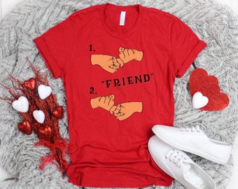 May include: Red t-shirt with a graphic of two hands making a pinky promise. The text "1. " and "2. " are above the hands, and the text "FRIEND" is in between the hands.