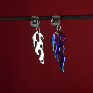 May include: Two silver hair clips with flame-shaped charms. One charm is silver and the other is iridescent blue and purple.