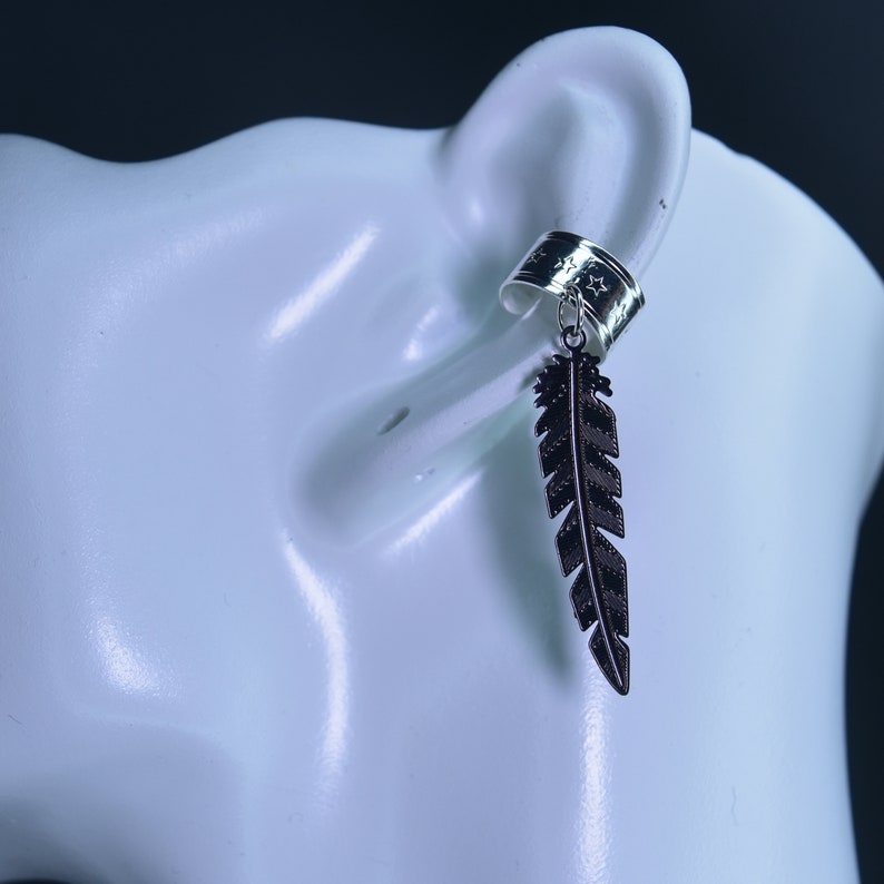 May include: A silver ear cuff with a black feather charm. The cuff has a star pattern and the feather is detailed with lines.