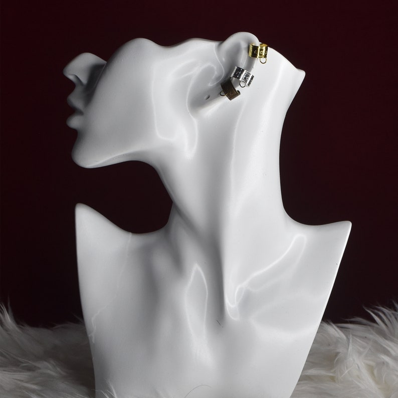 May include: A white mannequin head with a gold and silver ear cuff on the right ear.