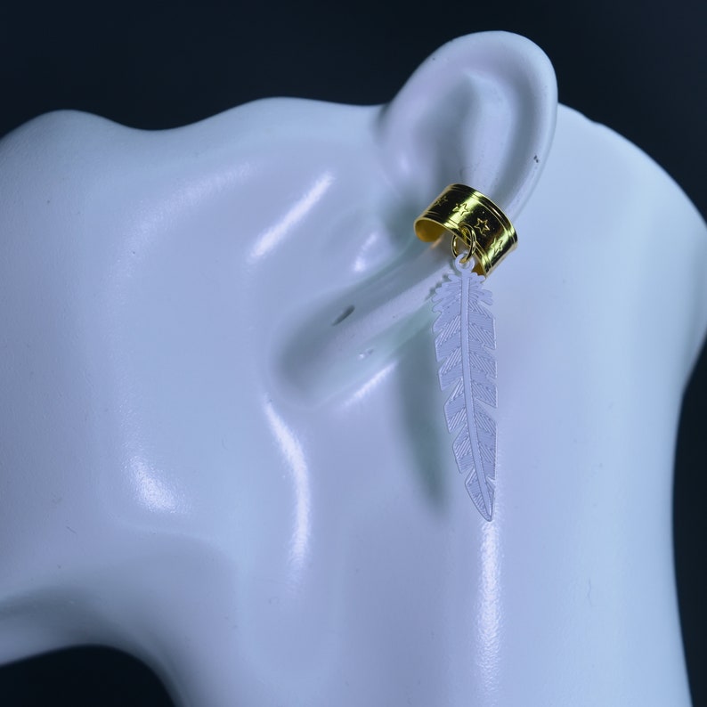 May include: A gold ear cuff with a white feather charm. The ear cuff is designed to fit on the upper part of the ear.