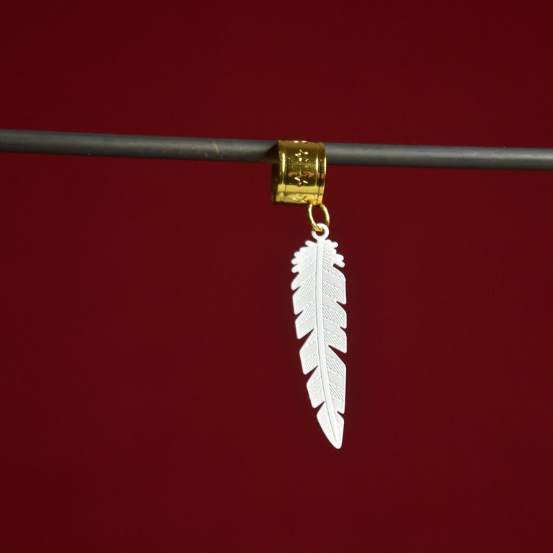 May include: A gold feather hair clip with a white feather charm. The feather charm is detailed with a textured design.