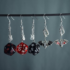 Può includere: Cinque paia di orecchini con catene e ciondoli d'argento. I ciondoli includono una chitarra, un pipistrello, una zanna e due dadi. I dadi sono rossi, neri e trasparenti.
