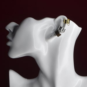 May include: Three ear cuffs in gold, silver, and brown metal. The cuffs are worn on a white mannequin head.