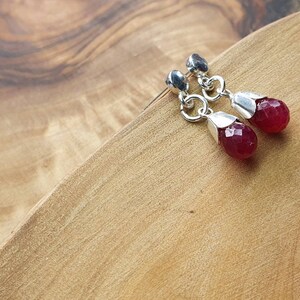 May include: A pair of silver earrings with red gemstone drops. The earrings have a delicate design and are perfect for adding a touch of elegance to any outfit.