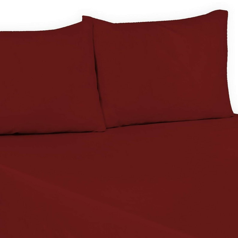 May include: Two burgundy pillowcases and a burgundy fitted sheet. The sheet is folded over the pillowcases.