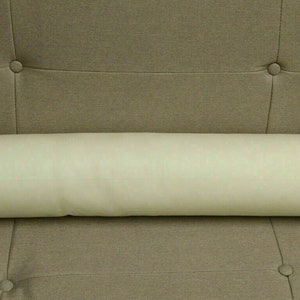 May include: A long, off-white bolster pillow resting on a brown sofa.