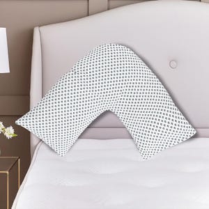 K&ouml;nnte beinhalten: Ein wei&szlig;es, V-f&ouml;rmiges Kissen mit einem sich wiederholenden Muster aus kleinen, dunkelblauen floralen Designs. Das Kissen liegt auf einem wei&szlig;en Bett, mit einem hellrosa Kopfteil im Hintergrund. Das Kissen ist f&uuml;r Komfort und Unterst&uuml;tzung konzipiert.