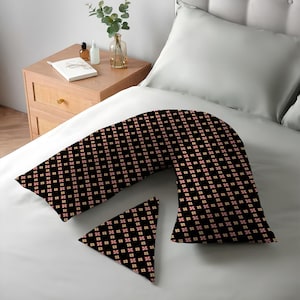 K&ouml;nnte beinhalten: Ein schwarzes K&ouml;rperkissen und ein kleines dreieckiges Kissen mit einem sich wiederholenden Blumenmuster in Rot und Creme. Die Kissen liegen auf einem wei&szlig;en Bett. Ein Nachttisch ist im Hintergrund.