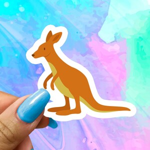 May include: A cartoon kangaroo sticker with a brown body and a white outline. The kangaroo is standing on its hind legs with its tail curled behind it. The sticker is on a colorful background.