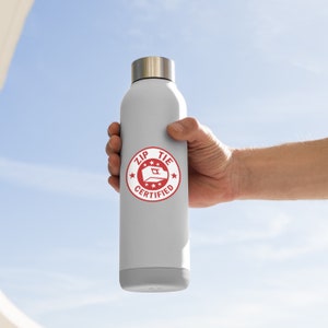 May include: A white water bottle with a red circle sticker that says "Zip Tie Certified" with a white star on each side of the text and a white zip tie icon in the center.