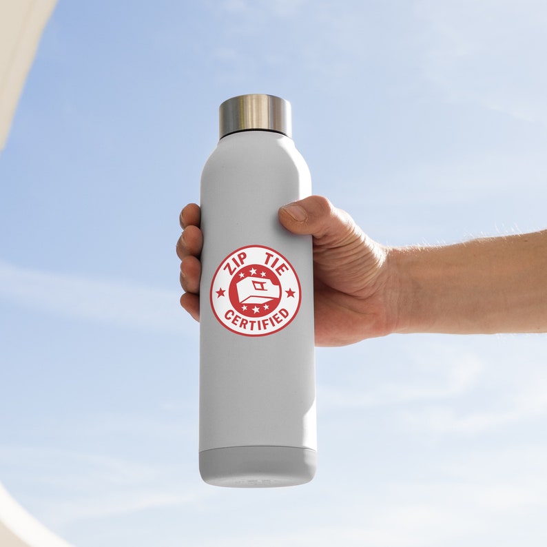 May include: A white water bottle with a red circle sticker that says "Zip Tie Certified" with a white star on each side of the text and a white zip tie icon in the center.