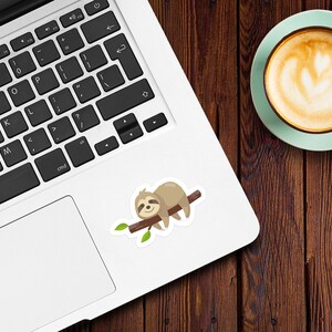 May include: A brown sloth with a white belly is sleeping on a branch with green leaves. The sloth is on a white laptop computer.