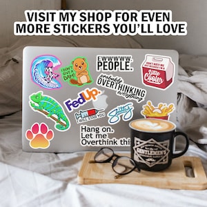 May include: A laptop computer covered in colorful stickers. The stickers feature various designs, including a cartoon beaver, a chameleon, a syringe, a paw print, a wave, and a cooler. The text on the stickers includes "Ewwww People", "Fed Up", "I Will Stab You", "Hang On", "Let Me Overthink This", "Cowabunga", "I Don't Give A Dah", "Don't Hate Me Just Because I'm A Little Cooler", and "Probably Overthinking Everything".