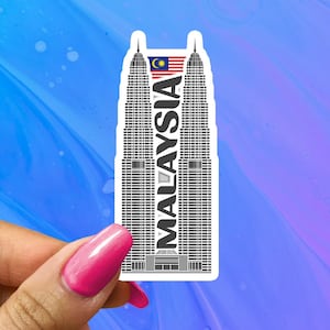 May include: A white sticker with a black and white illustration of the Petronas Towers in Kuala Lumpur, Malaysia. The word "MALAYSIA" is written vertically on the sticker, and a small Malaysian flag is in the upper left corner.