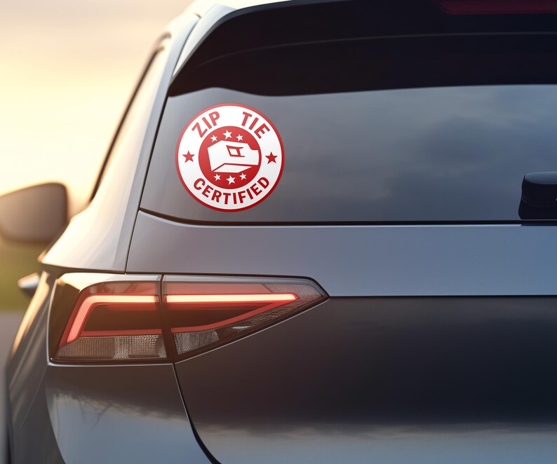 May include: A red and white sticker with the text "ZIP TIE CERTIFIED" and a stylized image of a zip tie. The sticker is on the back window of a gray car.