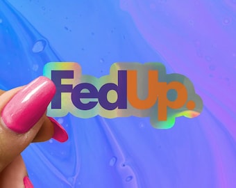 May include: A holographic sticker with the text "FedUp." in purple and orange letters. The sticker is being held by a hand with pink nail polish.