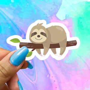 May include: A white sticker with a cartoon illustration of a brown sloth hanging from a branch with green leaves. The sloth has a happy expression and is hanging upside down.