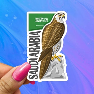 May include: A sticker featuring a brown and white falcon perched on a rock with the text "Saudi Arabia" and the Saudi Arabian flag in the background.
