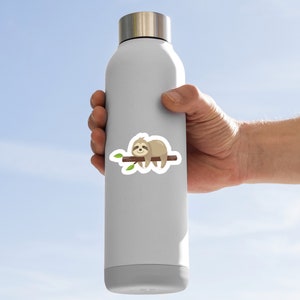 May include: A white water bottle with a sticker of a cartoon sloth sleeping on a branch. The sloth is brown with a light brown belly and has a small smile on its face.