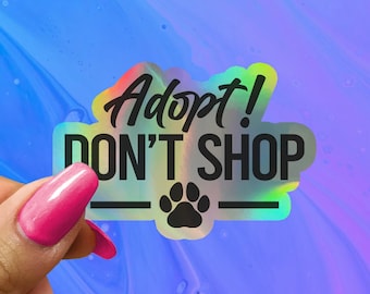 May include: A holographic sticker with the text "Adopt! Don't Shop" in black lettering. A black paw print is below the text.
