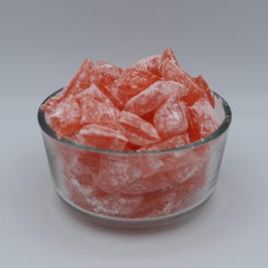 May include: A glass bowl filled with pink and white hard candies. The candies are shaped like small, irregular triangles and are covered in a fine white powder.