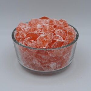 May include: A glass bowl filled with orange rock candy. The candy is in the shape of small, irregular diamonds.