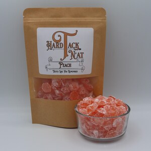 May include: A brown paper bag with a label that reads "Hard Tack N'at Peach" and a clear window showing peach flavored hard candies. The candies are in a glass bowl and are a light orange color.