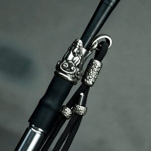 Peut inclure: Gros plan sur une pipe à eau noire et argentée. La pipe présente des détails argentés ornés, notamment une tête de dragon décorative et des accents texturés sur les fixations du tuyau. Le tuyau noir est relié à un tube en métal argenté.