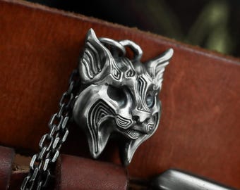 May include: A silver-colored pendant necklace featuring a stylized cat face. The pendant has intricate carved details and is suspended from a linked chain. The cat's face has a detailed design with visible ears, eyes, and a nose.