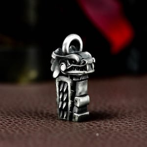 Könnte beinhalten: Ein silberfarbener Anhänger mit einem detaillierten Drachenkopf-Design auf einem rechteckigen Körper. Der Drache hat scharfe Zähne und einen wilden Ausdruck. Der Anhänger hat eine Schlaufe zum Befestigen an einer Kette. Das Design ist aufwendig und detailliert.