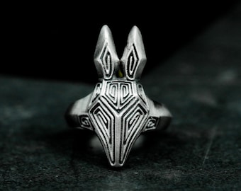 May include: A silver ring featuring a stylized Anubis design. The ring has a detailed, geometric pattern on the head and a smooth band. The Anubis head has pointed ears and a long snout, set against a dark background.