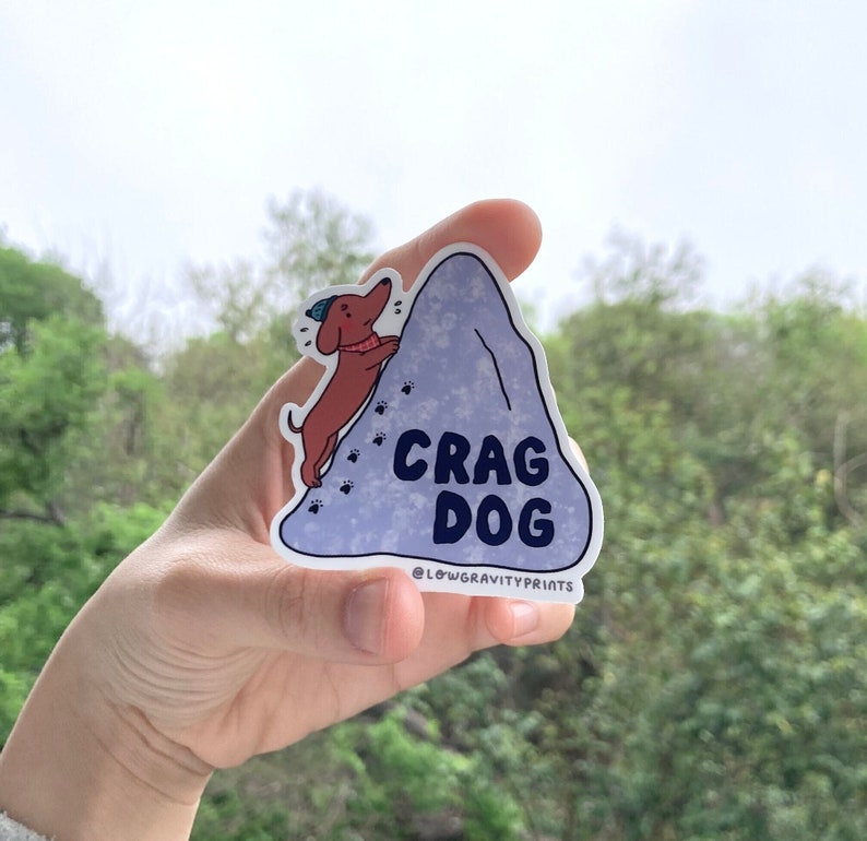 Sticker of a dachshund aka wiener hotdog climbing a boulder, beanie, chalky rocks, paw prints, dog that climbs outdoor, rock climbing, puppy adorable, vinyl, cragcat, crag cats, pet lovers, dogsofinstagram, hiking outside, steep sloper rocks,kawaii