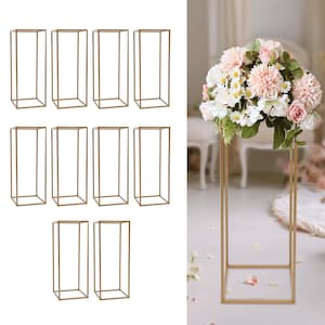 May include: Gold metal rectangular flower stands. The stands are open on all sides and are designed to hold floral arrangements. The image shows a variety of the stands, some empty and some holding flowers. The stands are a warm gold color.