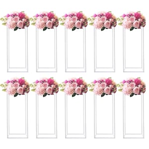 May include: Ten white metal floral stands, each topped with a bouquet of pink and light pink roses, hydrangeas, and greenery. The floral arrangements are arranged on rectangular stands, creating an elegant display for events.