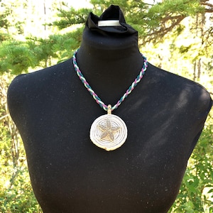May include: A silver necklace with a braided cord in green, white, and pink. The pendant is a round silver disc with a starfish design.