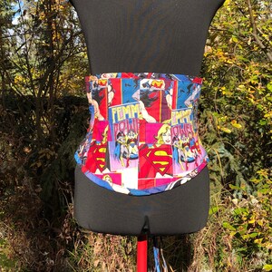 May include: A black corset with a colorful comic book print featuring female superheroes. The print includes the words "Femme Power" and images of Wonder Woman and Superman.