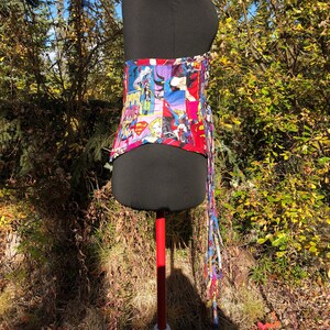 May include: A black corset with a colorful print of superhero characters. The corset has a long, colorful lace-up back.