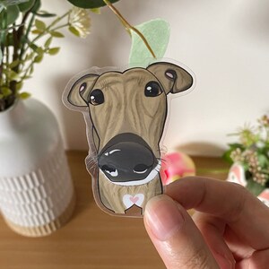 May include: A clear sticker of a brown and white dog with a pink heart on its chest. The dog is looking directly at the camera with its tongue out.