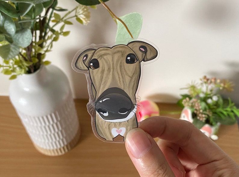 May include: A clear sticker of a brown and white dog with a pink heart on its chest. The dog is looking directly at the camera with its tongue out.